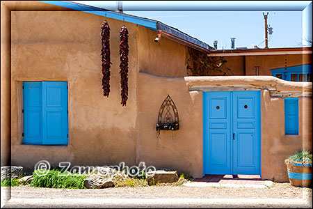 Adobehaus mit blauen Fensterläden und Türen und zwei Chilly Schoten an der Hauswand