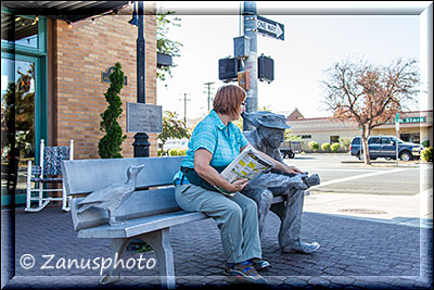 Auf Bank sitzende Skulptur mit Tourist daneben