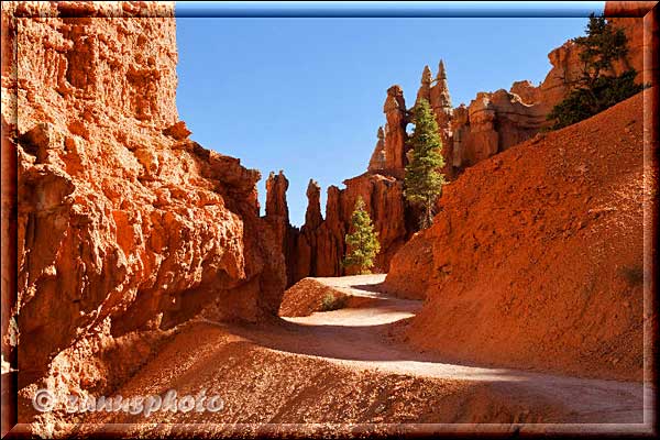 Trail verläuft durch hohe rote Felswände.