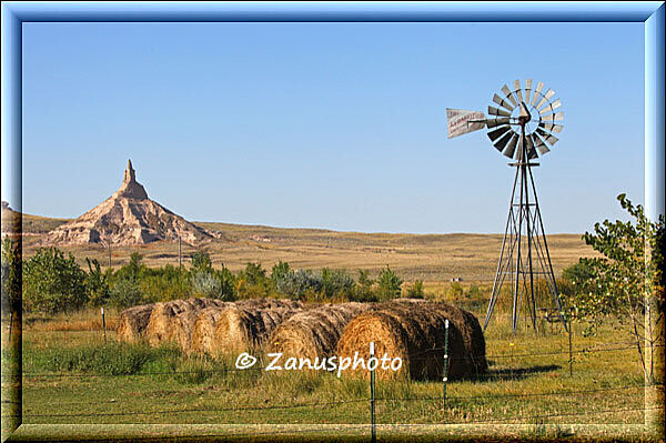 Nebraska, Strohrollen im Vordergrund, ein Windrad und der Chimney Rock dahinter